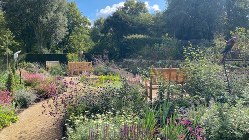View across a colourful summer garden with a pond and bench